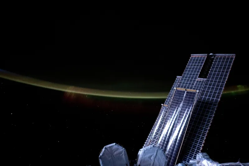 Solar array wings of the International Space Station above Earth's glowing limb (NASA)
